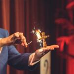 A magician lights a straw man that is standing in his left palm