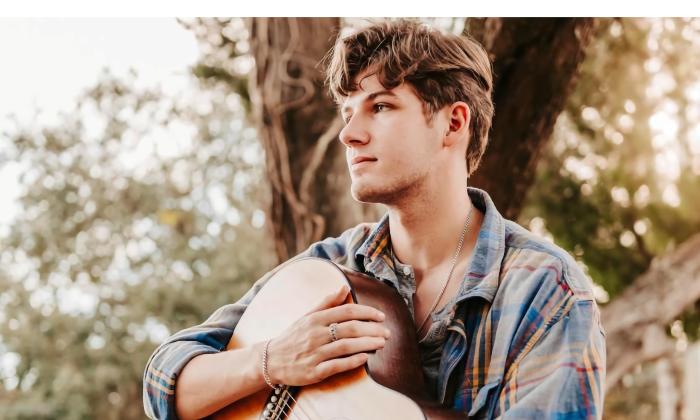 Musician Damon Slaughter with his guitar, sitting outside near trees