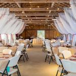 The interior of the barn venue space at Florida Agricultural Museum, decorated for a wedding with draped fabric and round tables