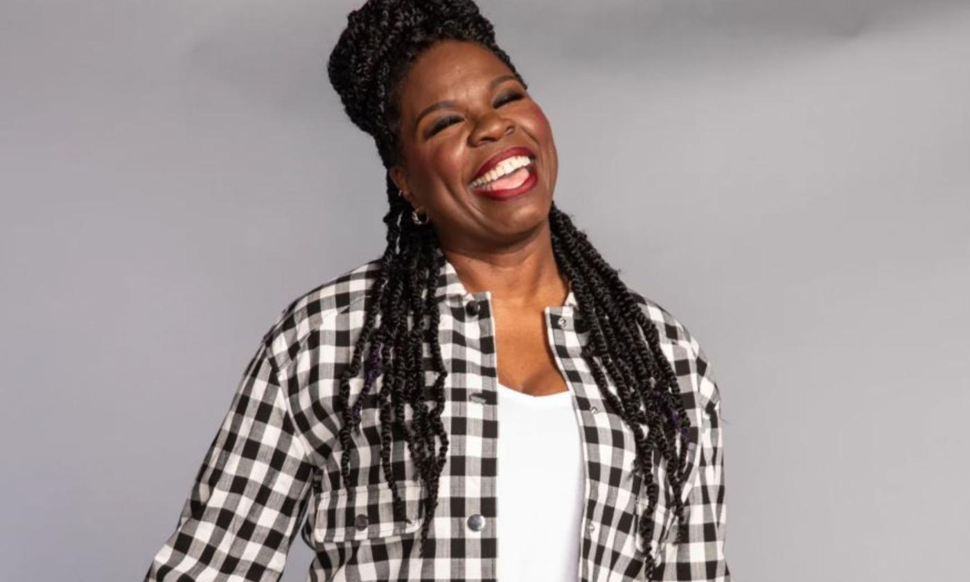 Comedian Leslie Jones smiles in front of a grey backdrop. 