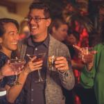 Audience members prior to the Magic Hideaway show, smiling and holding signature cocktails