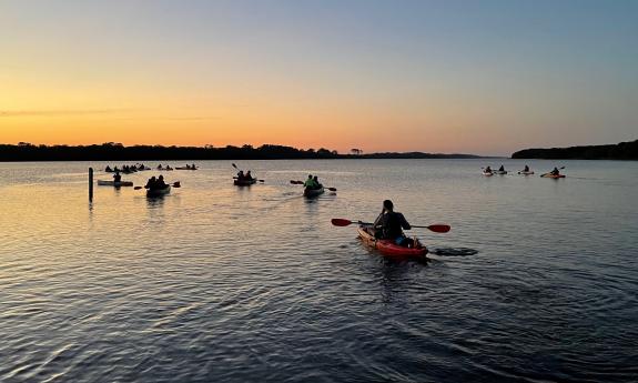 People paddling kayaks toward the sunset in Guana