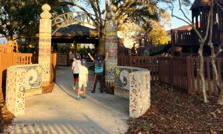 Little kids with Visit St. Augustine baseball hats on walking under Project Swing playground sign in St. Augustine.