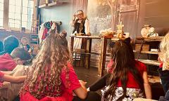 Children sitting in a local museum listening to a woman wearing colonial clothing